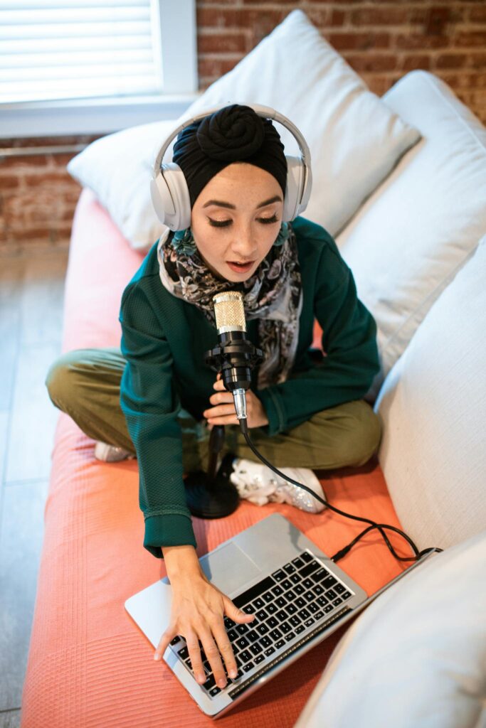 Young woman recording a podcast using laptop and microphone at home.